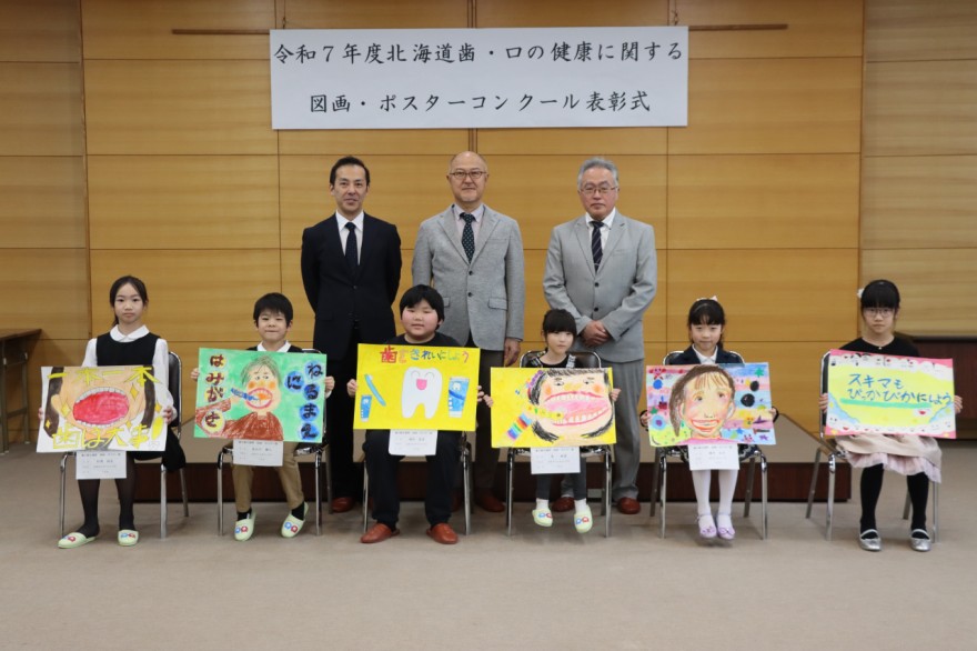 受賞作品を手にする児童と岩井会長（後列中央）ら関係者