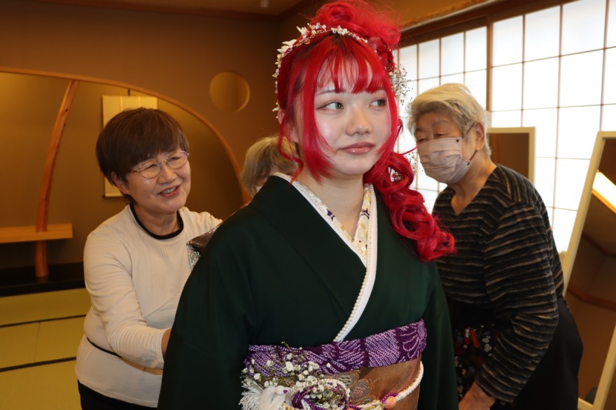 「七飯の街並みに着物姿をふやす会」メンバーに振袖を着付けてもらう参加者（七飯町）