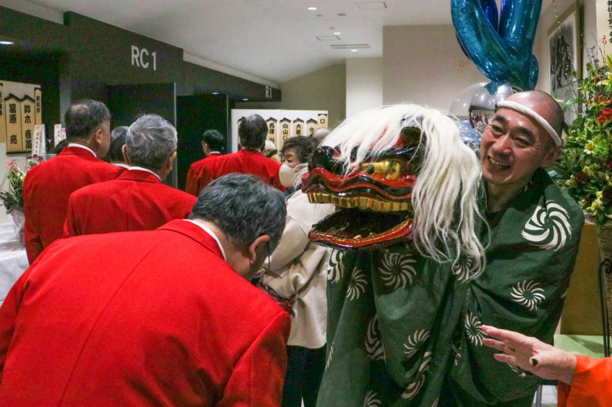 開場から幕開けまでロビーで来場者や出演者の頭を噛んで邪気払いをした獅子舞（ワタナベヒロシさん、右）